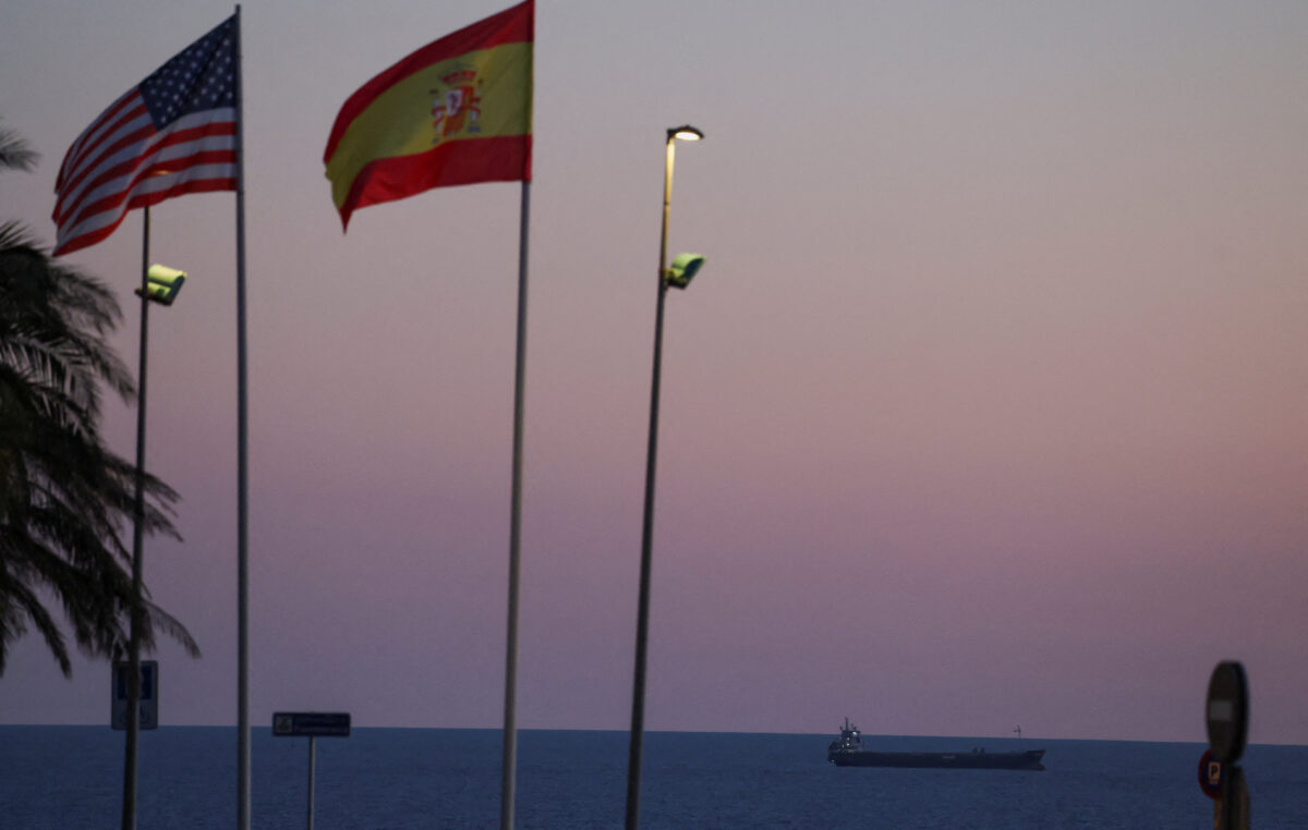 A cargo ship is anchored near the port of Algeciras at sunset, behind the flags of the United States and Spain on a roundabout near the jointly operated naval base in Rota, in the province of Cadiz, Spain March 15, 2026. REUTERS/Nacho Doce