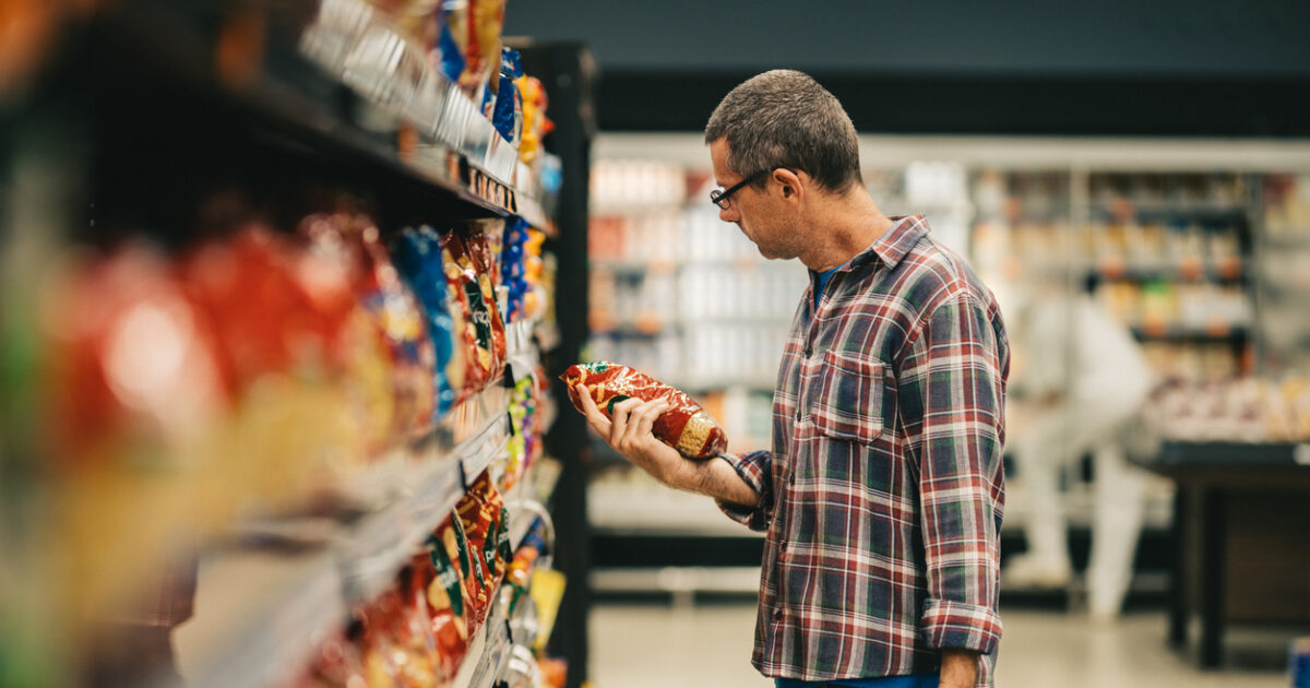 Man standing in a supermarket aisle and reading the label on a bag of pasta while grocery shopping