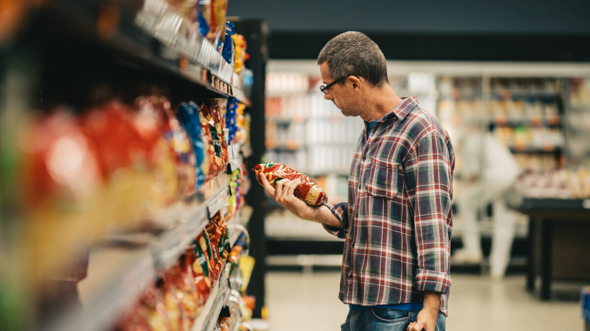 Man standing in a supermarket aisle and reading the label on a bag of pasta while grocery shopping