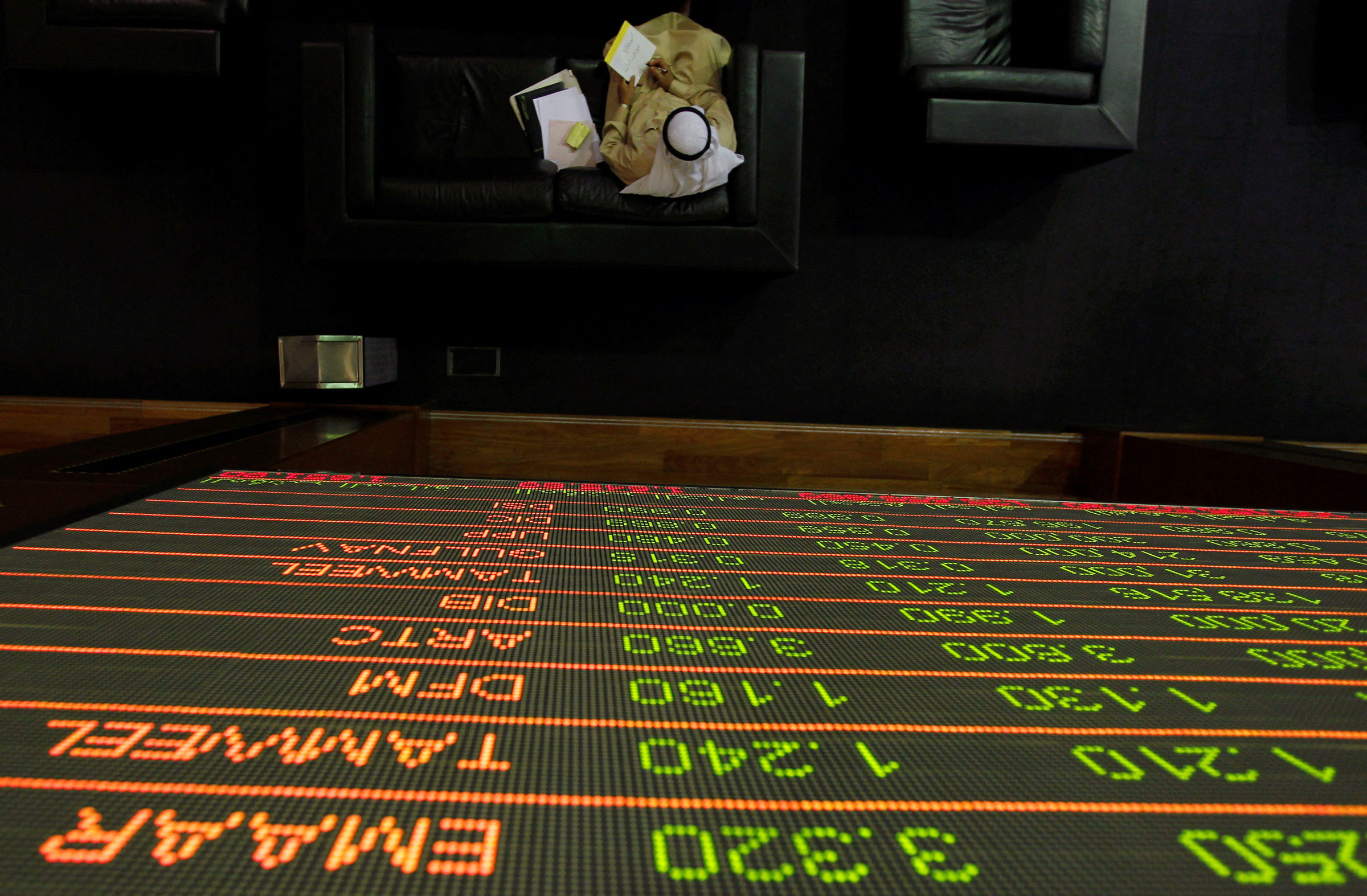 FILE PHOTO: A stock exchange information is seen on a screen is seen as a man works on the trading floor at the Dubai Financial Market April 29, 2012. REUTERS/Jumana El Heloueh/File Photo
