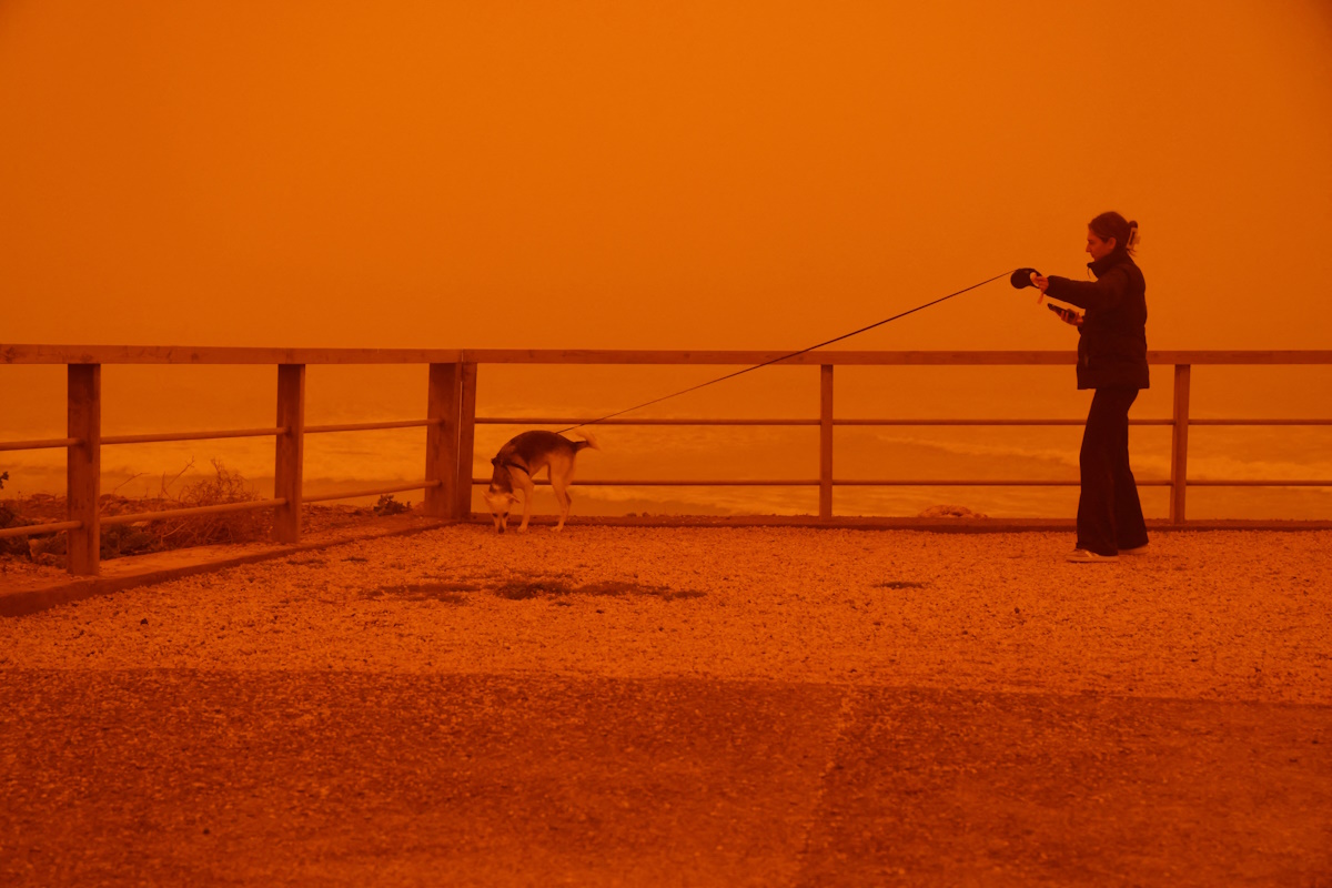 A woman walks her dog amid a haze caused by sand dust from the Sahara, due to strong southern winds, in Heraklion, Crete island, April 1, 2026. REUTERS