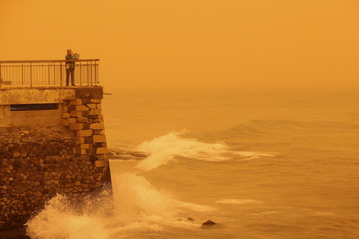 A woman takes pictures of the horizon turned yellow, caused by sand dust from the Sahara, due to strong southern winds, in Heraklion, Crete island, Greece April 1, 2026. REUTERS