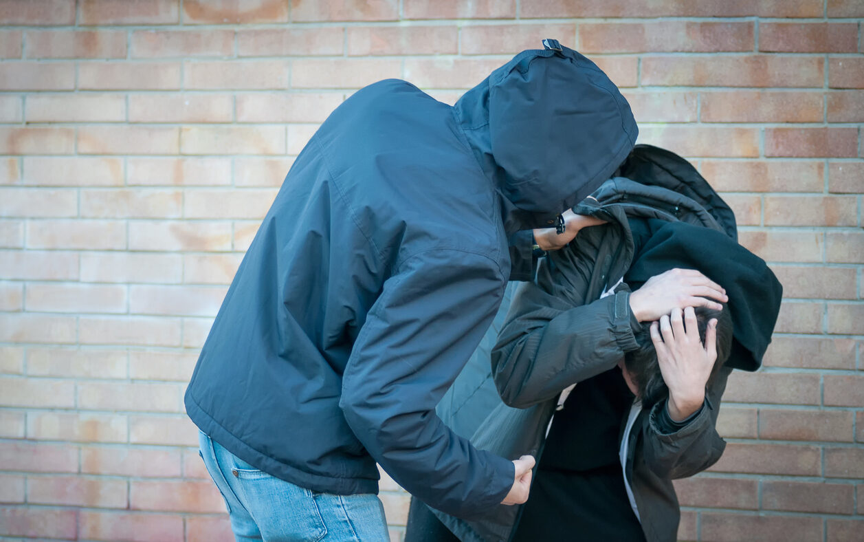 Bullying, aggression and violence scene between two males, one young adult male punches his peer near a bricks wall