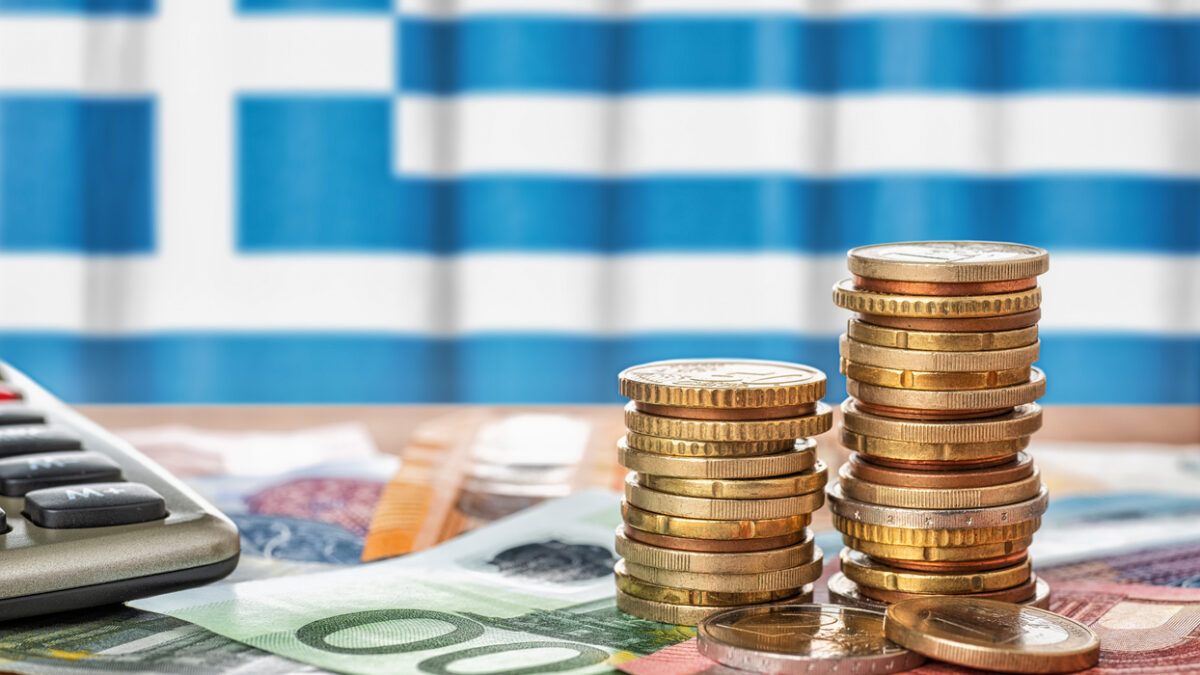 Euro banknotes and coins in front of the national flag of Greece