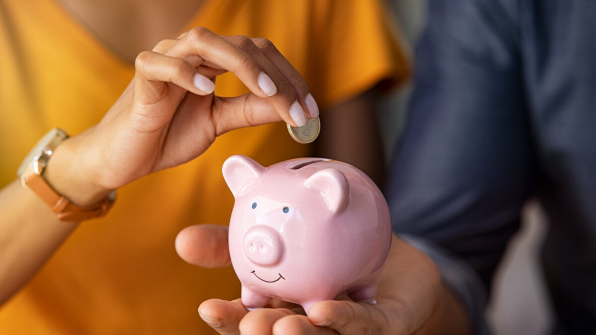 Close up of man holding pink piggybank while woman putting coin in it. Indian young couple saving money for their wedding. Close up of woman hand putting euro money in piggy bank to save for the purchase of an house.