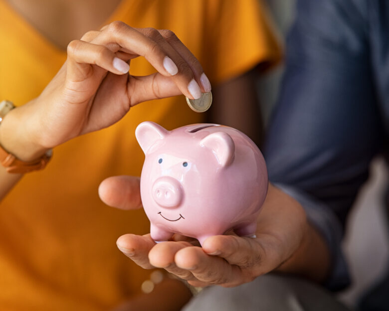 Close up of man holding pink piggybank while woman putting coin in it. Indian young couple saving money for their wedding. Close up of woman hand putting euro money in piggy bank to save for the purchase of an house.