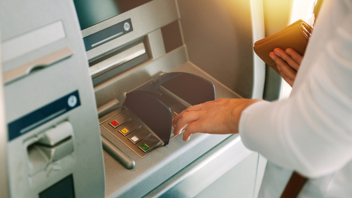 Woman using ATM holding wallet an pressing the PIN security number on the keyboard automatic teller machine