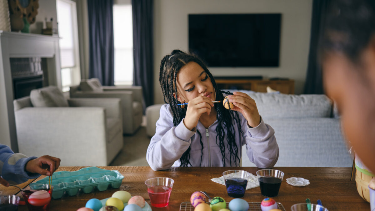 Young girls sitting at a home table, dyeing and decorating Easter eggs.