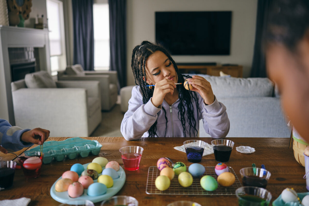 Young girls sitting at a home table, dyeing and decorating Easter eggs.
