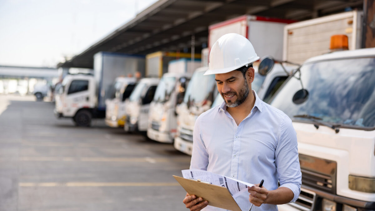 Happy Latin American woman working as a supervisor at a distribution warehouse and looking at documents on a clipboard