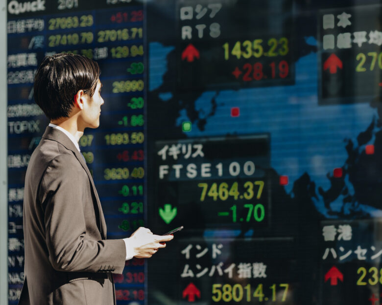 Confirm the stock price of the world on the outdoor electronic bulletin board with a smartphone in hand in the 30s Japanese businessman