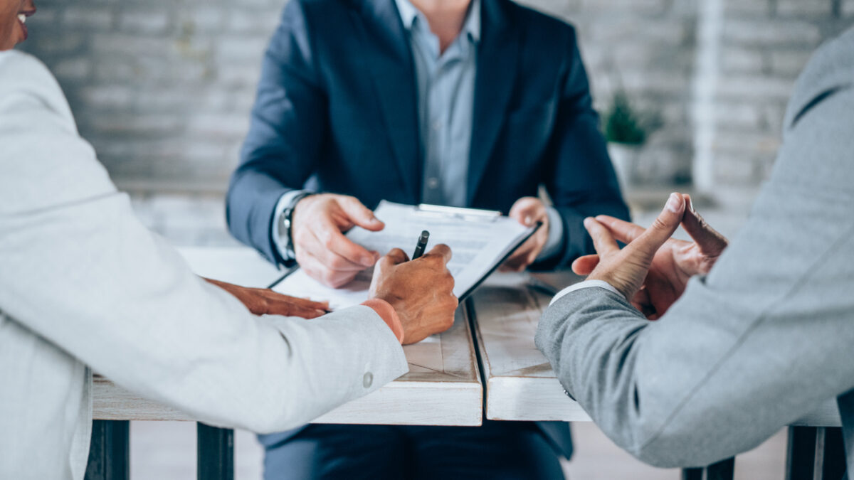 Couple sitting at desk in the bank and signing loan agreement. Shot of three business persons filling in paperwork in an office. Business persons signing a document in board room.