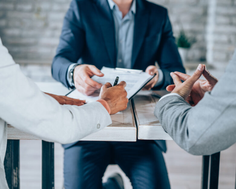 Couple sitting at desk in the bank and signing loan agreement. Shot of three business persons filling in paperwork in an office. Business persons signing a document in board room.
