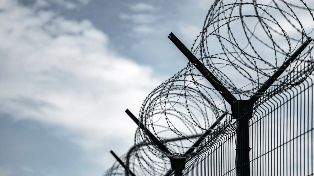 Barbed Wire Fence. Prison or border fence with razor wire against dark sky. Security concept