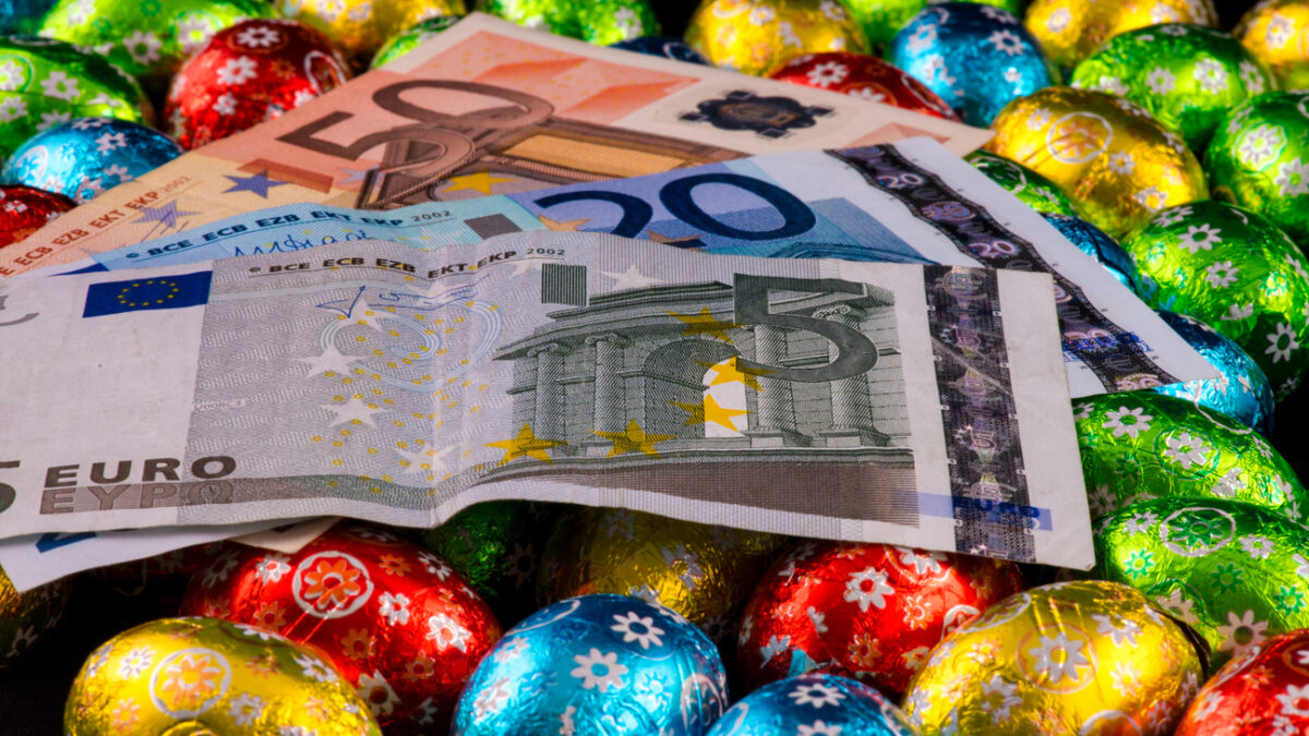 Easter. Consumerism. Close up of money and colorful chocolate eggs.