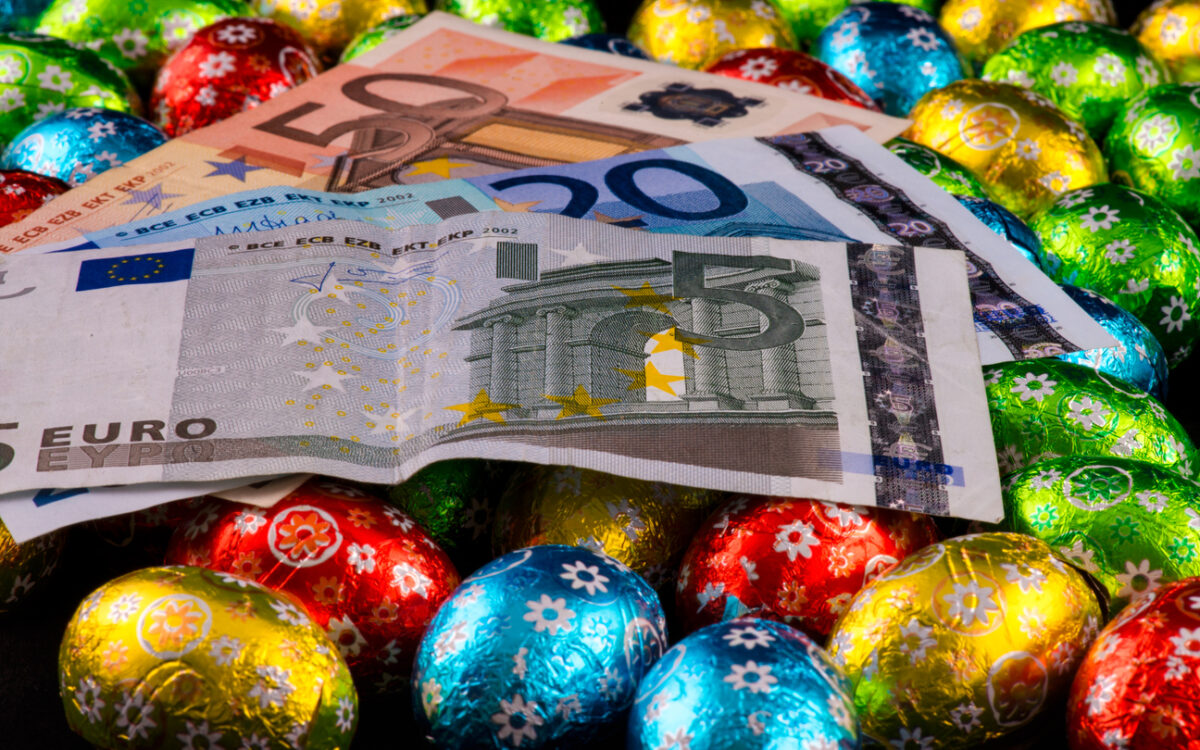 Easter. Consumerism. Close up of money and colorful chocolate eggs.