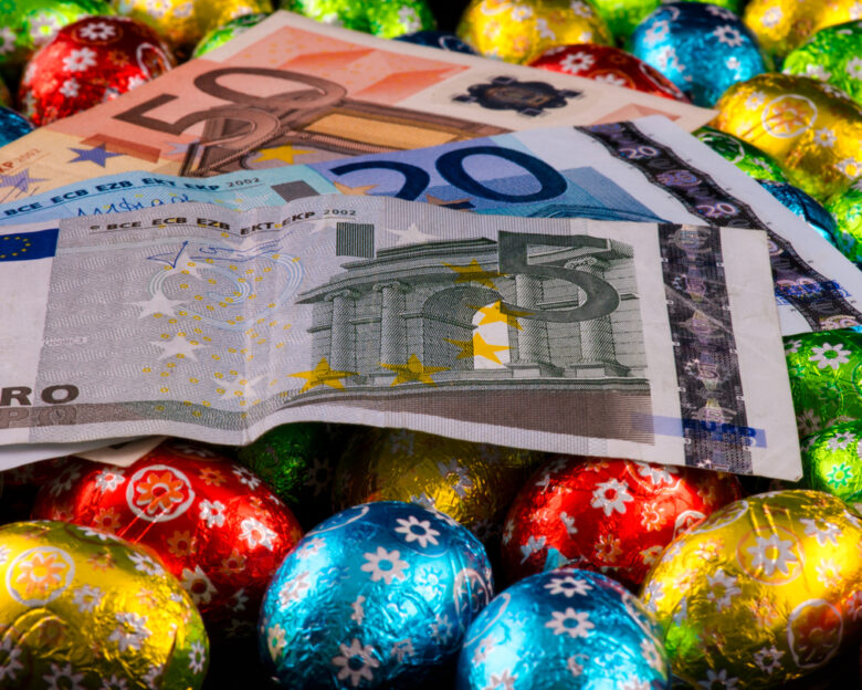 Easter. Consumerism. Close up of money and colorful chocolate eggs.