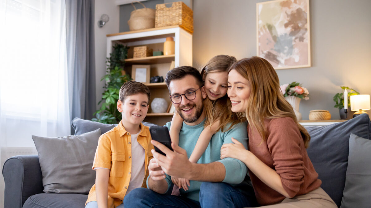 Capturing a cosy, home scene where a happy family with a mother, father, and kids engaging with a mobile phone, enjoying their time together