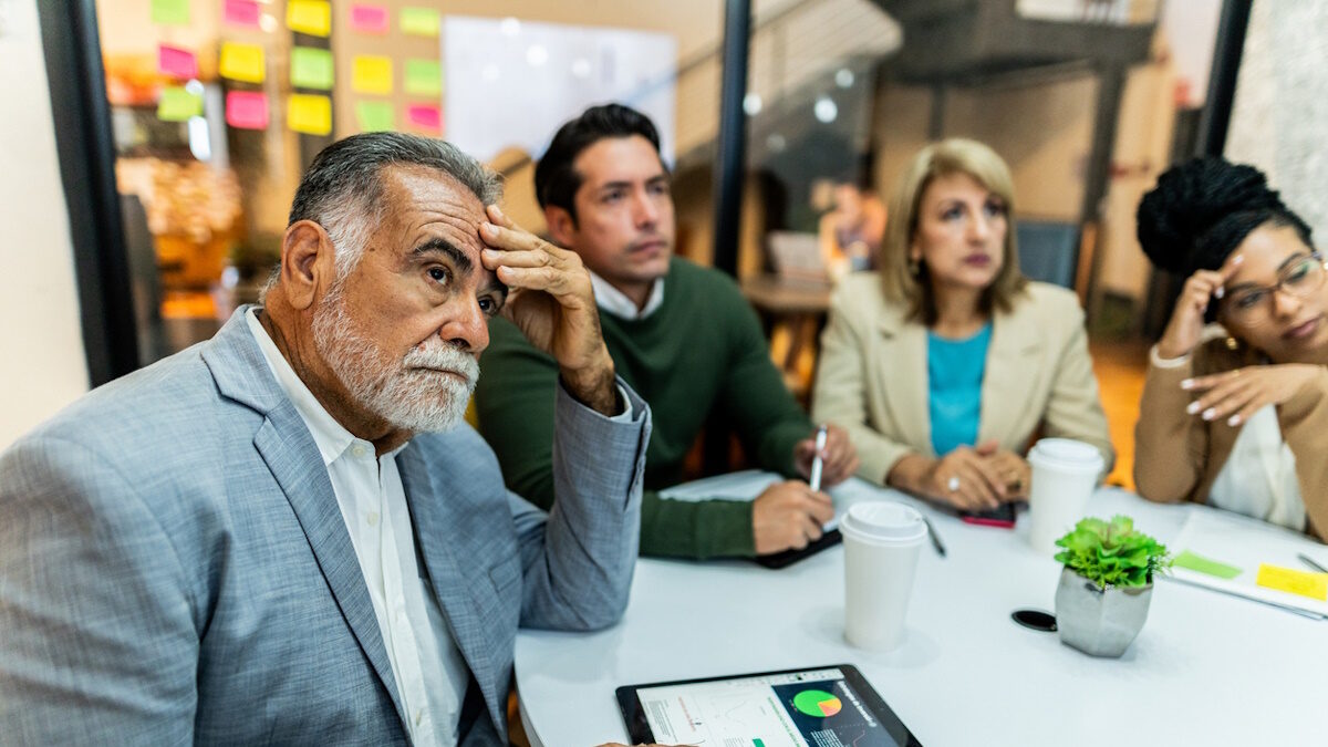 Worried senior businessman listening presentation with coworkers during business meeting at office