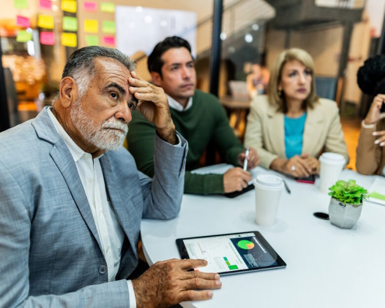 Worried senior businessman listening presentation with coworkers during business meeting at office
