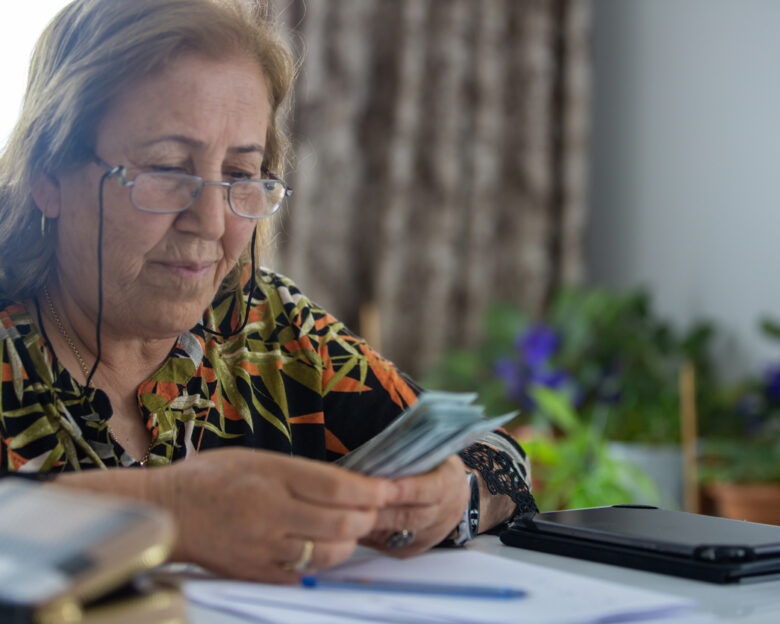 Old woman counting money at the table while sitting in the living room