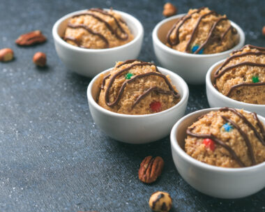Safe-to-eat raw monster cookie dough in small portion bowl and nuts on dark blue background. Ideas and recipes for kids and toddlers meal. Copy space for text.