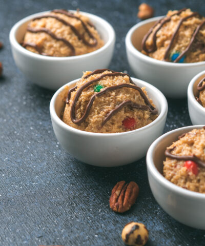 Safe-to-eat raw monster cookie dough in small portion bowl and nuts on dark blue background. Ideas and recipes for kids and toddlers meal. Copy space for text.