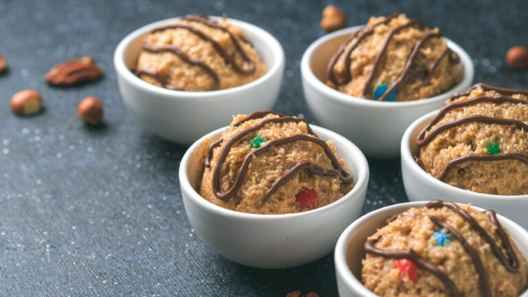 Safe-to-eat raw monster cookie dough in small portion bowl and nuts on dark blue background. Ideas and recipes for kids and toddlers meal. Copy space for text.