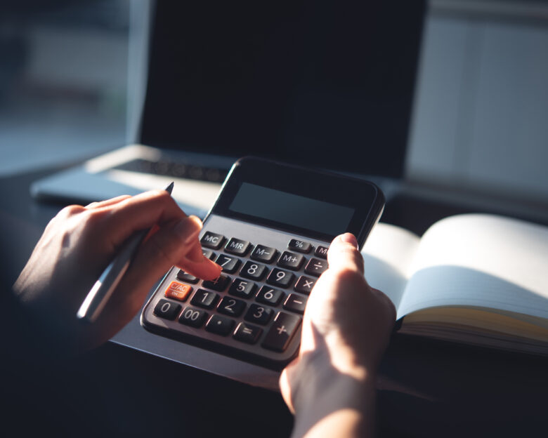 Close up, business woman working at office, using calculator to calculate company finance, accounting with laptop computer on table, budget management. Doing home finance, budgeting and tax calculation