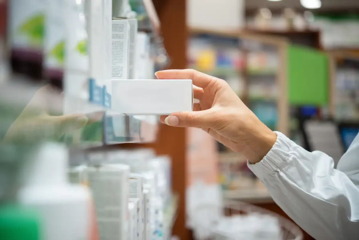 Pharmacist taking medicine box from shelf in a pharmacy