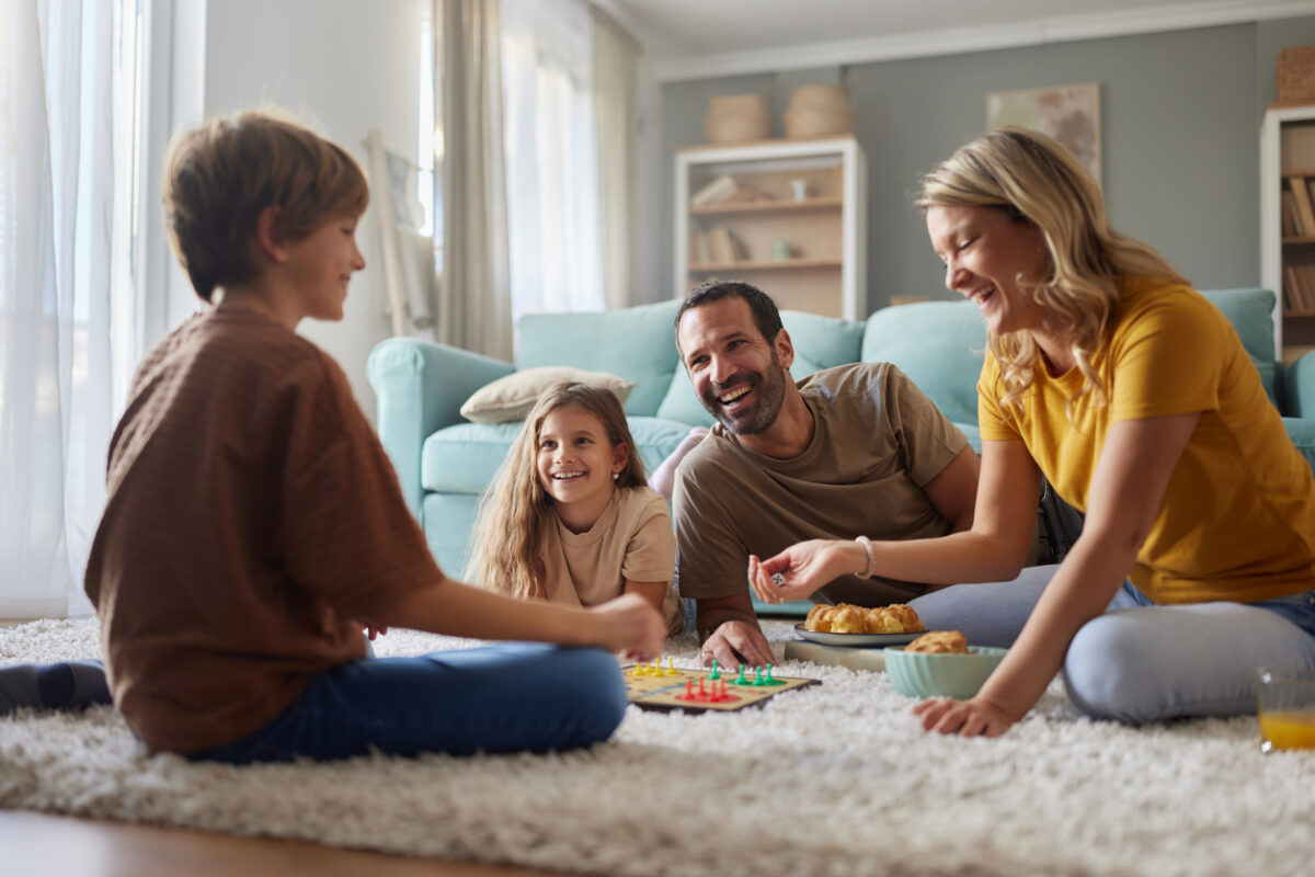 Happy family having fun while playing Ludo game on carpet in the living room. Focus is on father and daughter.