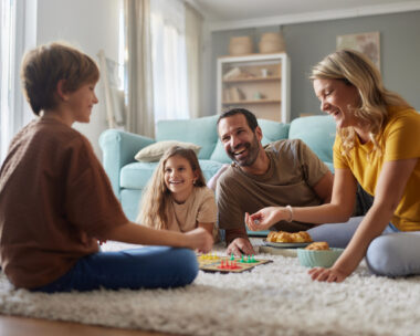 Happy family having fun while playing Ludo game on carpet in the living room. Focus is on father and daughter.