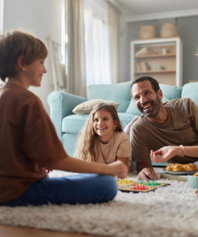 Happy family having fun while playing Ludo game on carpet in the living room. Focus is on father and daughter.