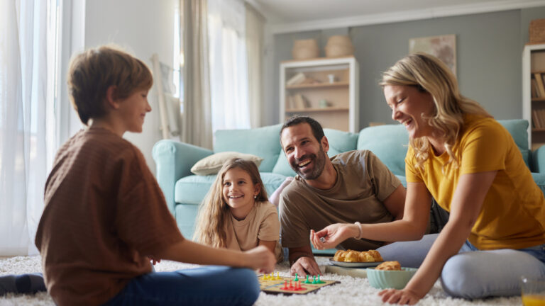 Happy family having fun while playing Ludo game on carpet in the living room. Focus is on father and daughter.