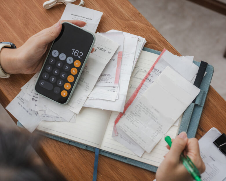 Close up a woman managing her home finances with a smartphone, she reviews financial bills. Concepts include financial planning, taxes, spending, budgeting, and financial challenges.