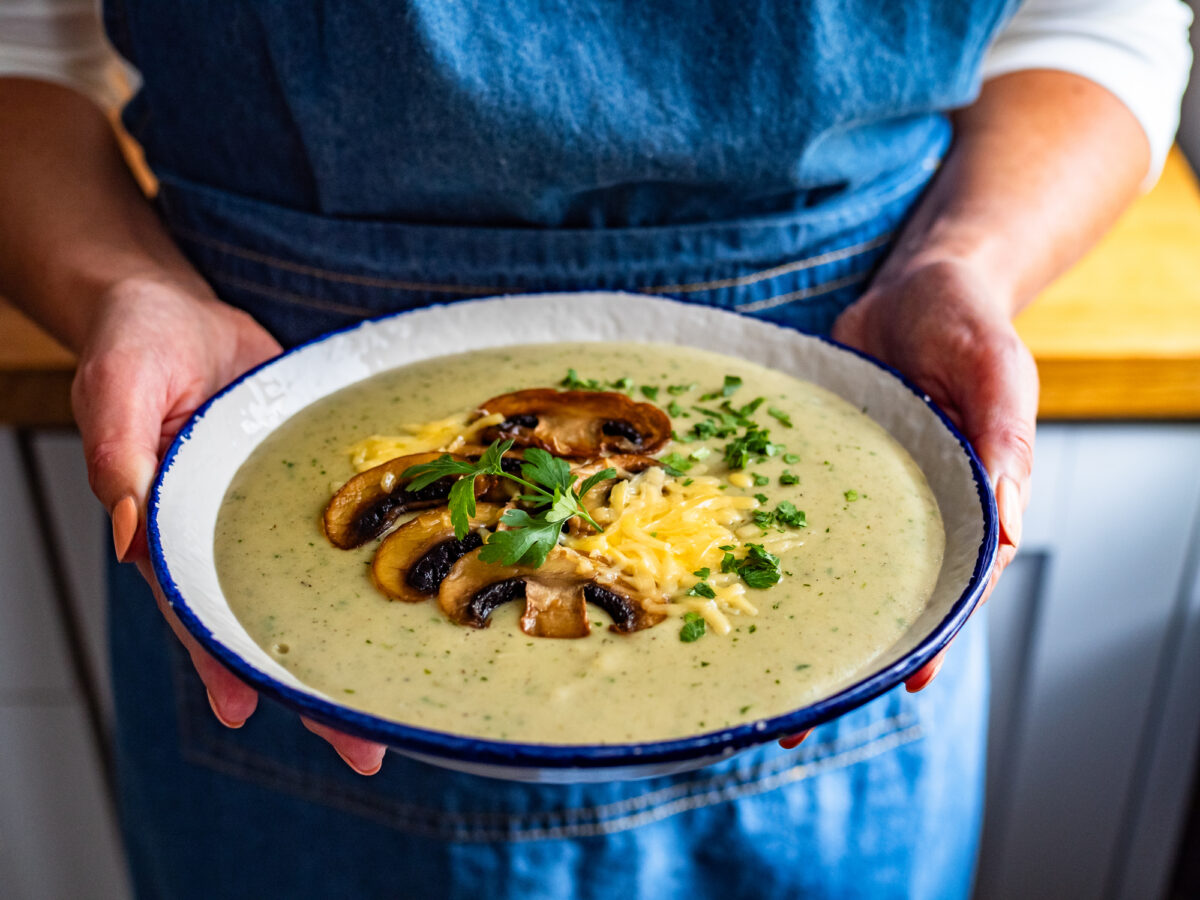 Woman holding bowl with creamy mushroom soup, close-up