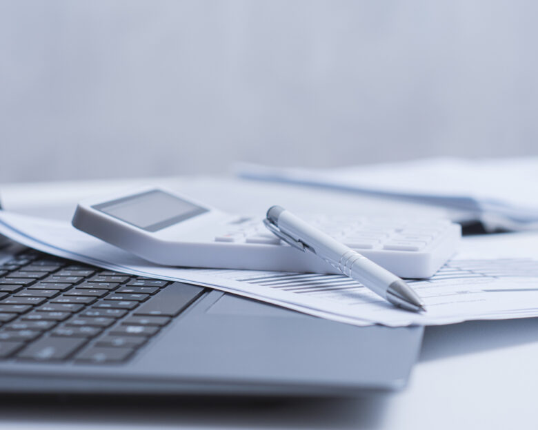 Calculator and pen placed on a white office desk with financial documents and laptop. Clean modern workspace concept for accounting, finance, budgeting and business analysis