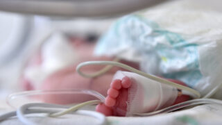 Newborn baby with cannula in the feet on a hospital bed