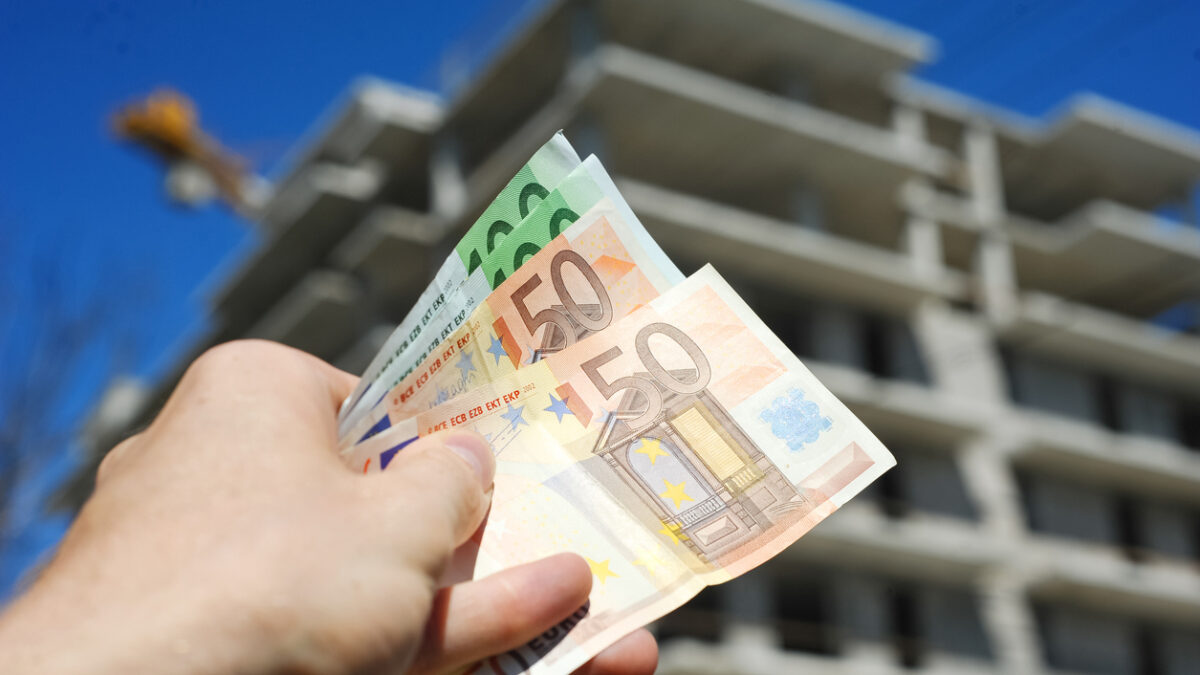 Man holding euro money in front of block building in build process
