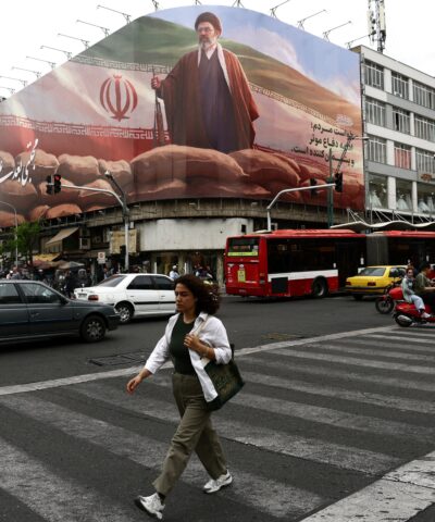 Γυναίκα περπατάει μπροστά από μία τεράστια πινακίδα του νέου ηγέτη του Ιράν Μοτζτάμπα Χαμενεΐ