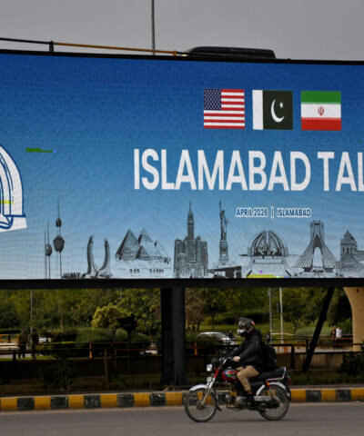 FILE PHOTO: A man rides his motorbike past a billboard installed alongside a road as Pakistan prepares to host the U.S. and Iran for peace talks, in Islamabad, Pakistan, April 10, 2026. REUTERS/Waseem Khan/File Photo