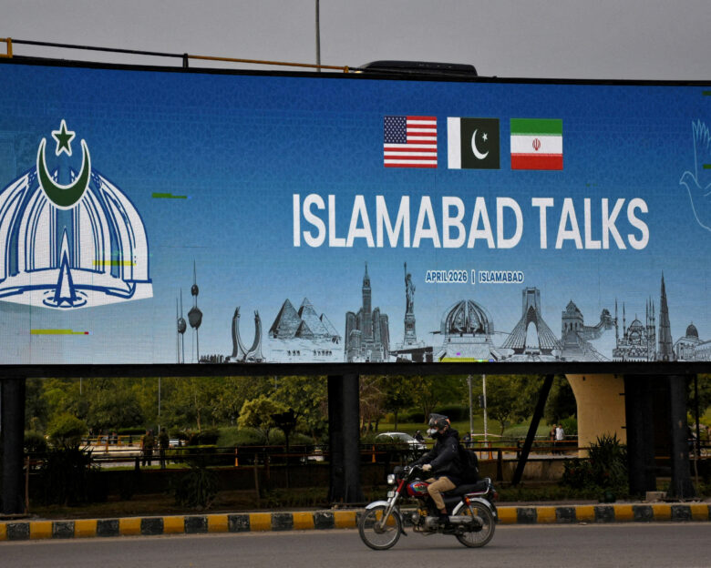 FILE PHOTO: A man rides his motorbike past a billboard installed alongside a road as Pakistan prepares to host the U.S. and Iran for peace talks, in Islamabad, Pakistan, April 10, 2026. REUTERS/Waseem Khan/File Photo