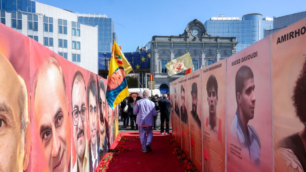 Άντρας περπατάει με μία σημαία δίπλα σε φωτογραφίες κρατουμένων που εκτελέστηκαν στο Ιράν