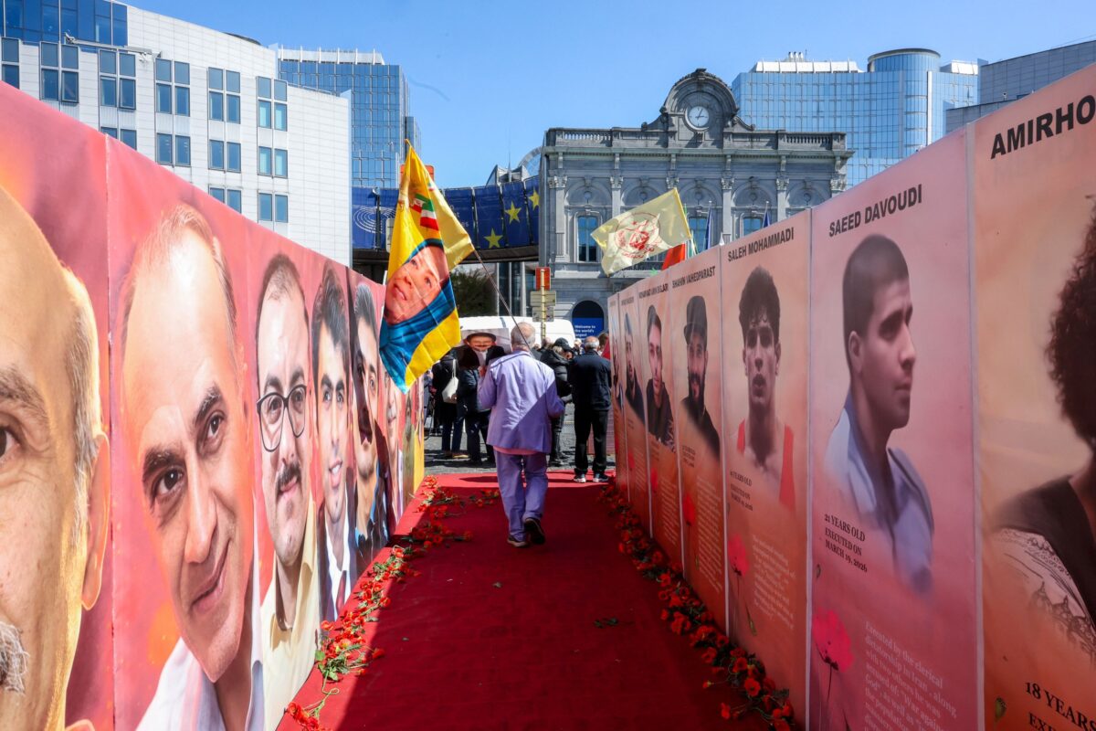 Άντρας περπατάει με μία σημαία δίπλα σε φωτογραφίες κρατουμένων που εκτελέστηκαν στο Ιράν