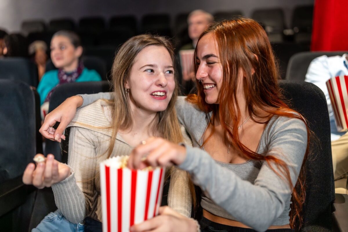 Two female friends enjoying a movie night, sharing popcorn and laughs, creating a joyful and memorable cinema