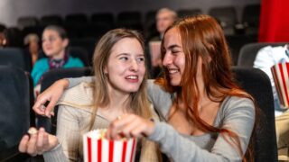 Two female friends enjoying a movie night, sharing popcorn and laughs, creating a joyful and memorable cinema