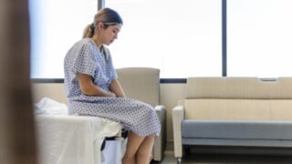 The anxious, sad, young female patient wears her gown as she waits in the hospital room.