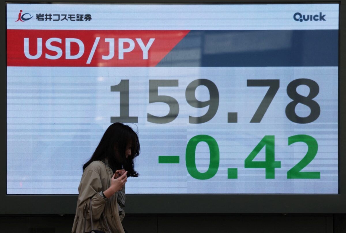 A woman walks past a screen displaying the exchange rate between Japanese yen and U.S. dollar outside a brokerage in Tokyo, Japan, March 30, 2026. REUTERS/Issei Kato