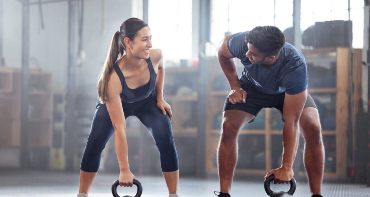 Strong, wellness couple doing kettlebell weight exercise, workout or training inside a gym. Happy sports people or trainer motivation, exercising with fitness equipment for muscle, strength or health