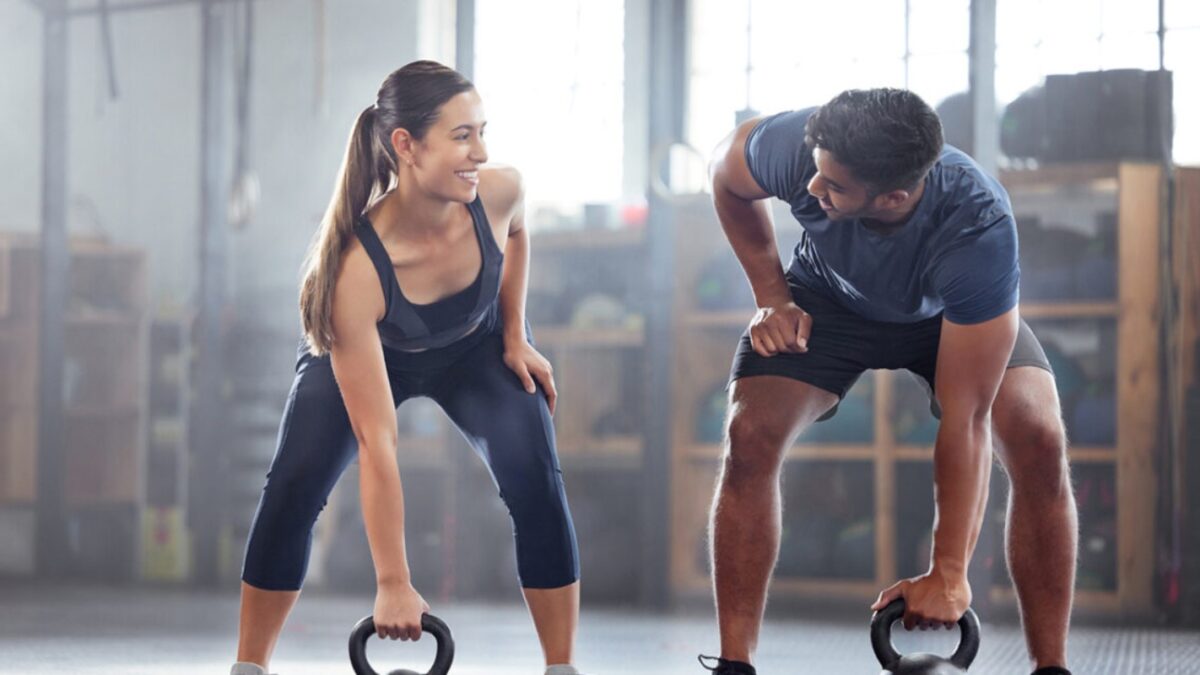 Strong, wellness couple doing kettlebell weight exercise, workout or training inside a gym. Happy sports people or trainer motivation, exercising with fitness equipment for muscle, strength or health